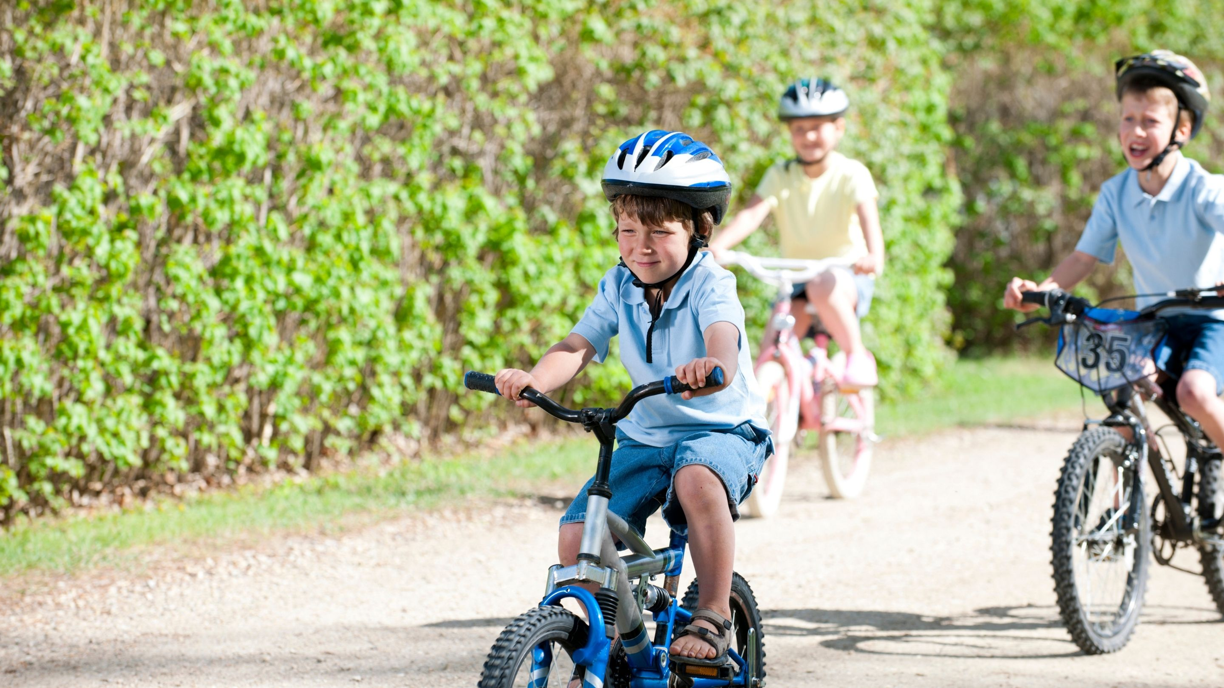 Vaikai su dviračiais ir šalmais važiuoja keliu